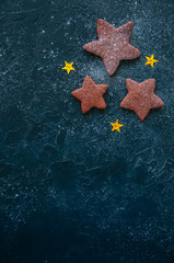Different sized three gingerbread chocolate star cookies on a black stone background.