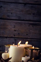 Lit candles and dry leaves on table