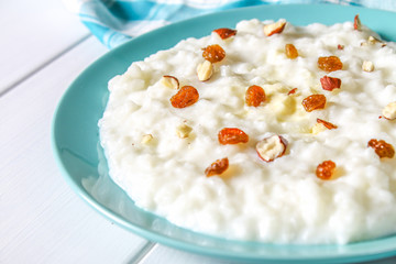 Rice milk porridge with nuts and raisins in a blue dish on a white wooden table.