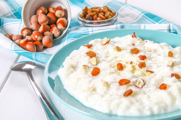 Rice milk porridge with nuts and raisins in a blue dish on a white wooden table.