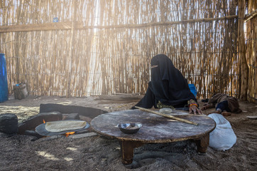 Egypt, Bedouin Village, August 28, 2017: Muslim woman, sitting by the hearth bakes traditional bread for the family