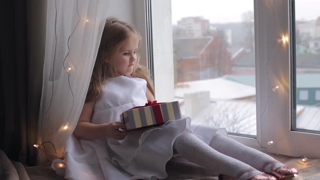 Dreaming young girl with gift sitting on a windowsill