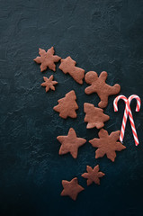 Chocolate gingerbread cookies and candy canes on a black stone backdrop. Top view and copy space.