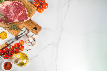 Fresh raw meat, lamb beef marble steak on a cutting board, with ingredients for cooking. On white marble table, copy space top view