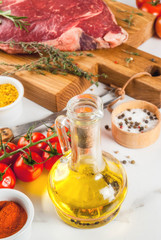 Fresh raw meat, lamb beef marble steak on a cutting board, with ingredients for cooking. On white marble table, copy space