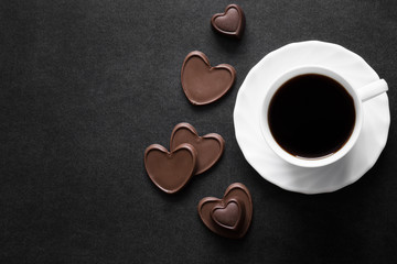 Cup of black coffee with chocolate hearts on the dark table. Enjoying a coffee and candies with beloved on the date. Empty place for a text.