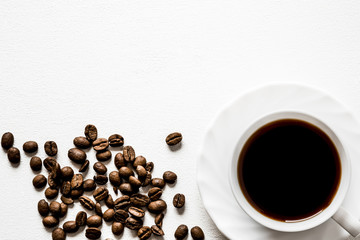 Cup of coffee with brown beans on the white table. Enjoying of coffee break at the work, at home, at visit with friends, family or alone everyday. Choice of the best sort and quality coffee.