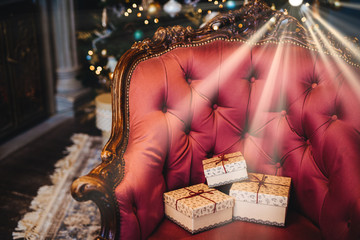 Horizontal picture of wrapped three gift boxes on beautiful royal armchair indoors. Home interior. Celebration, holidays, present concept. Christmas presents decorated with ribbons