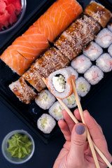 Popular Japanese food - Sushi rolls set with wasabi, ginger and chopsticks, top view. Female hands holding chopsticks with roll.