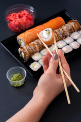 Popular Japanese food - Sushi rolls set with wasabi, ginger and chopsticks, top view. Female hands holding chopsticks with roll.