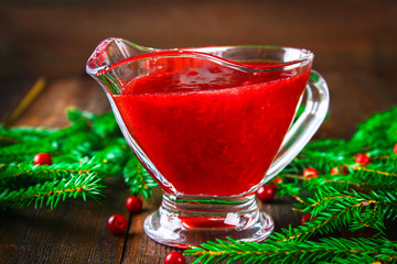 Cowberry cranberry sauce in a glass clear saucer on a wooden table with spruce branches.