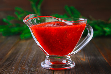 Cowberry cranberry sauce in a glass clear saucer on a wooden table with spruce branches.