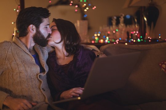 Couple kissing each other while using laptop in living room