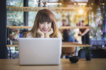 Beautiful happy young curly woman sitting in cafe and using laptop	