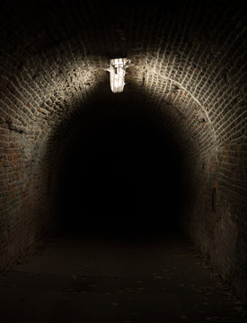Dark tunnel and corridor during night. Light is illuminating old historical pathway made of bricks. Spooky and frightening atmosphere of dark, gloomy and murky place.
