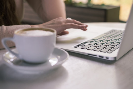 Close-up of a Woman sitting in at a table with a cup of coffee working on her laptop computer