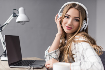 happy young woman listening music with headphones and looking at camera