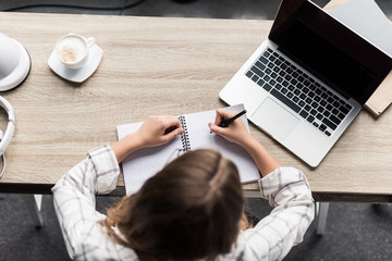 top view of young woman writing in notebook at workplace