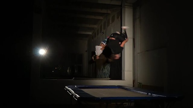 A pair of acrobats simultaneously do a somersault on a trampoline, slow motion