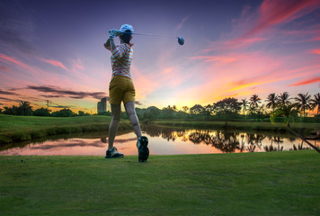a woman golf player in an action of ene of downswing after hit the golf ball away from tee off to...