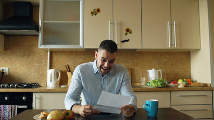 Handsome man recieve good news reading letter in the kitchen while have breakfast at home early morning