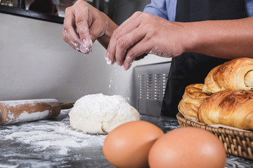 Close up of Man hands sprinkling flour over fresh dough with ingredients on black background