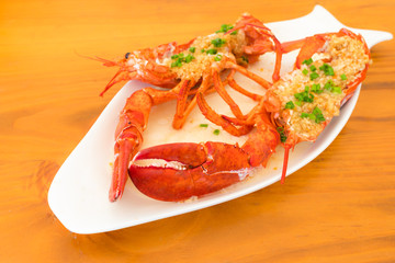 Red baked lobster with herbs on a white plate against the background of a wooden table