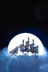 Sail ship in light of full moon. Wooden model on dark background. Conceptual marine still life.