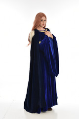  full length portrait of girl wearing long blue velvet gown and fur lined cloak, standing pose  on white background.