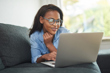 Smiling African woman lying on her sofa using a laptop