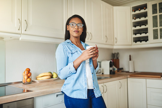 Young African Woman Standing In Her Kitchen Drinking Coffee