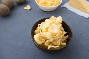 Potato chips with cheese in a plate that is located on a gray background.