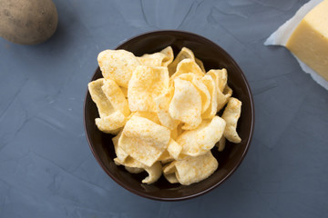 Potato chips with cheese in a plate that is located on a gray background.