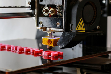 3D printer printing the words 3D technology in red letters, close up of the machine while printing with visible print head.