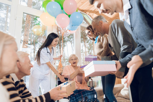 A group of young and old people in a nursing home congratulate an elderly woman on her birthday.
