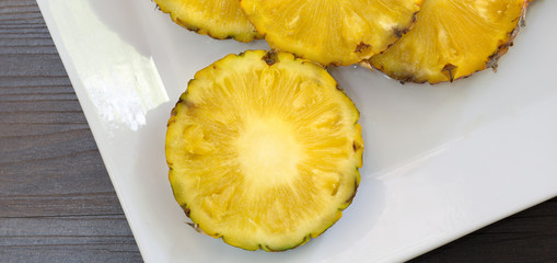 Pineapple slices with peel in white dish on wooden background