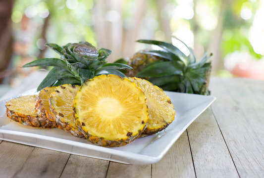 Pineapple slices with peel in white dish on wooden table in the garden