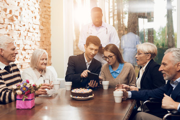 Young and old people sit together at the table in the room of a nursing home.