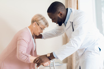 The doctor helps to get out of bed an elderly woman in a nursing home.