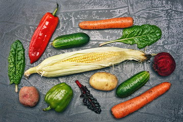 Vegetables on a gray structural background. Pepper, cucumber, corn, carrots, beets, potatoes, leaves of mangolt.