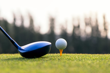 Close up golf ball and driver, player doing golf swing tee off on the green sunset evening time,...