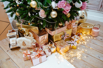 set of gold and silver gift boxes under a Christmas tree. Gifts lie on the wooden floor decorated with the shining garland.