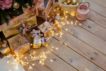 set of gold and silver gift boxes under a Christmas tree. Gifts lie on the wooden floor decorated with the shining garland.