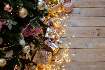 set of gold and silver gift boxes under a Christmas tree. Gifts lie on the wooden floor decorated with the shining garland.