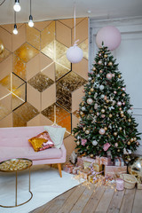 the room decorated by Christmas. A pink sofa and a big fir-tree with toys, spheres, garlands and gifts.
