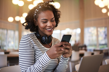 Smiling African college student reading text messages between cl