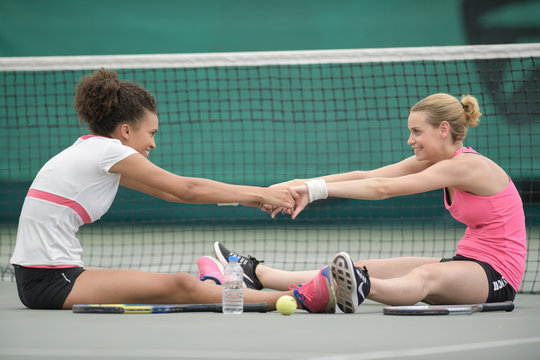 two attractive female tennis players stretching at the court