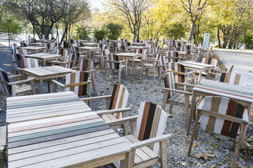 Fototapeta na wymiar Empty tables and chairs at park restaurant, cold autumn day. Autumn approach, season change concept 