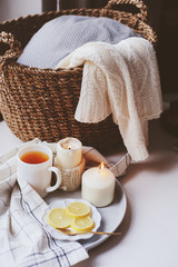 Cozy winter morning at home. Hot tea with lemon, candles, knitted sweaters in basket and modern metallic interior details. Still life composition, danish hygge concept