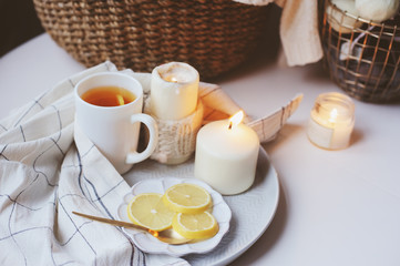 Cozy winter morning at home. Hot tea with lemon, candles, knitted sweaters in basket and modern metallic interior details. Still life composition, danish hygge concept